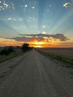 the sun is setting over an empty dirt road