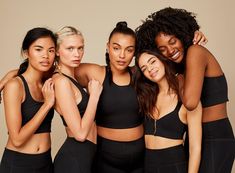 four women in black sports bras posing for the camera with their arms around each other