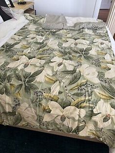 a bed with a floral comforter on top of it next to a night stand