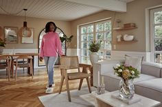 a woman in a pink sweater is walking through a living room with white furniture and wooden floors