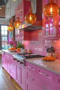 a kitchen with pink cabinets and oranges on the counter top, lights hanging from the ceiling