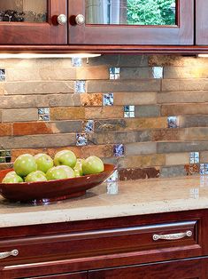 a bowl of green apples sitting on top of a counter next to a wooden cabinet