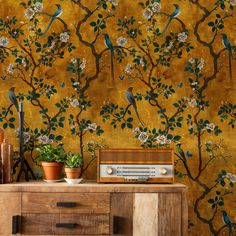 a wallpaper with birds and flowers on it, next to a wooden dresser in front of a yellow background