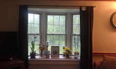 there is a clock on the wall above a window sill with flowers in it