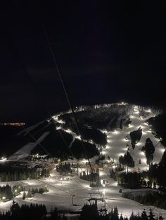 a ski slope at night with lights on it and trees in the foreground, lit up by streetlights