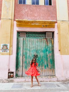 a woman standing in front of a green and yellow building with a red dress on