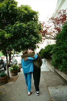 two people walking down a sidewalk with trees in the back ground and one person carrying another