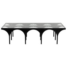 a black table with four legs that are shaped like an arch and have white designs on the top