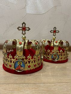 two gold crowns sitting on top of a wooden floor next to each other with crosses