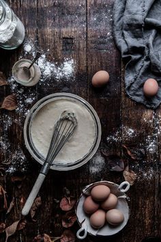 some eggs are sitting in a bowl next to other ingredients on a wooden table with spoons