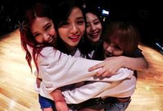 four girls hugging each other on a wooden floor in front of a television screen with lights