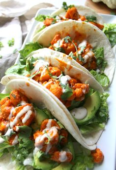 three tacos are on a white plate with lettuce and other toppings