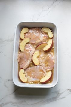 an apple and chicken dish in a white casserole dish on a marble countertop