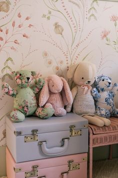 three stuffed animals sitting on top of two suitcases in front of a floral wallpaper