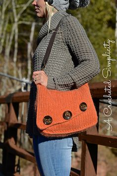 a woman is standing on a bridge with her purse in hand and wearing a knitted hat