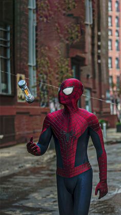 a man in a spider - man suit is walking down the street with an object in his hand