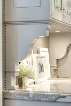 a white vase with flowers sitting on top of a marble counter next to a mirror