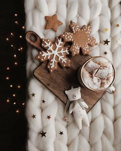 a wooden cutting board topped with cookies and marshmallows next to a cup of hot chocolate