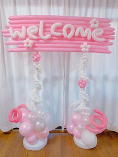 the welcome sign is decorated with balloons and streamers in pink, white and silver