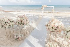 an outdoor wedding setup on the beach with white and pink flowers in vases at the end of the aisle