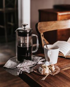 a wooden table topped with a cup of coffee next to an open book