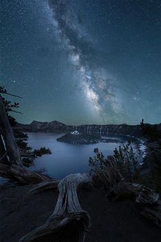 the night sky is filled with stars and clouds above a lake surrounded by trees in the foreground