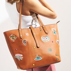 a woman carrying a brown handbag with stickers on it