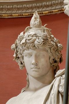 a statue of a woman holding a pole in front of a red wall with ornate carvings on it