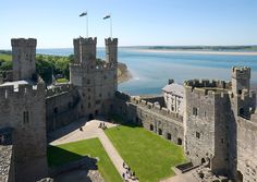 an aerial view of a castle with water in the background and people walking around it