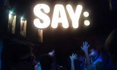 a group of people standing under a neon say sign