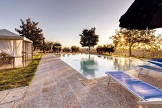 an empty swimming pool with lounge chairs next to it and trees in the background at sunset