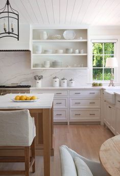 a kitchen with white cabinets and wood flooring next to a dining room table in front of a window