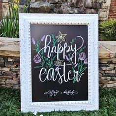 a chalkboard sign that says happy easter in front of a stone wall with flowers