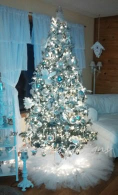 a white christmas tree in a living room with blue and silver decorations on the top