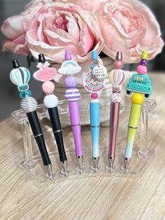 several pens are lined up on a table next to a pink rose and glass vase