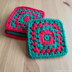 two square crocheted coasters sitting on top of a wooden table next to each other