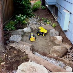 two toy trucks sitting in the middle of a yard with rocks and gravel around it