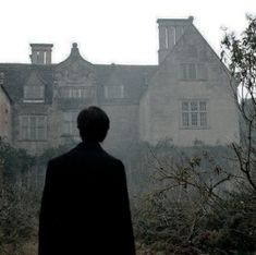 a man standing in front of an old building with trees and bushes around him looking at the sky