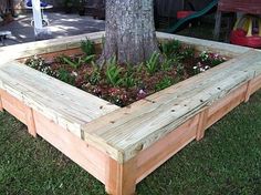 a wooden planter box sitting on top of grass next to a tree and fence