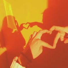 two hands making the shape of a heart in front of a yellow and red background