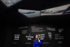 a woman standing in front of a black wall holding a cell phone to her ear