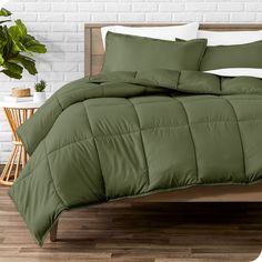 a bed with green comforter and pillows on it next to a potted plant