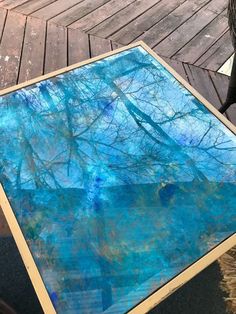 a table that has been painted with blue and green paint on it, sitting on a wooden deck