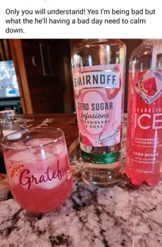 two bottles of gin on a counter top next to a glass with pink liquid in it