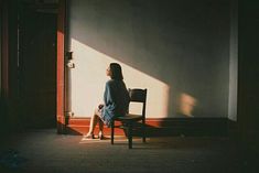 a woman sitting in a chair looking out the window with her shadow on the wall