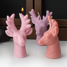 two candles with pink and purple deer heads next to each other on a white table