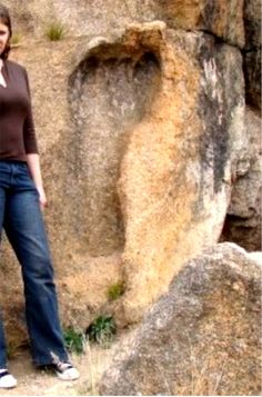 a woman is standing in front of some rocks talking on her cell phone and smiling