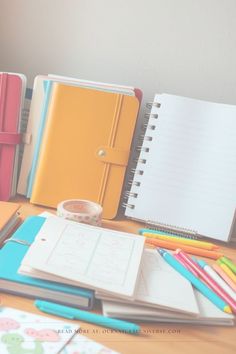 notebooks and pens are lined up on a desk next to an empty notepad