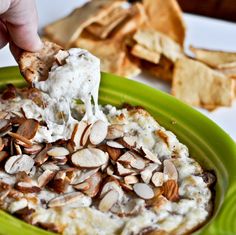 a person dipping some food into a green bowl with tortilla chips on the side