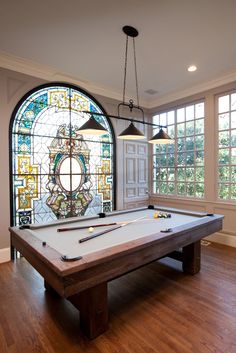 a pool table in front of a large stained glass window with two lights hanging from it